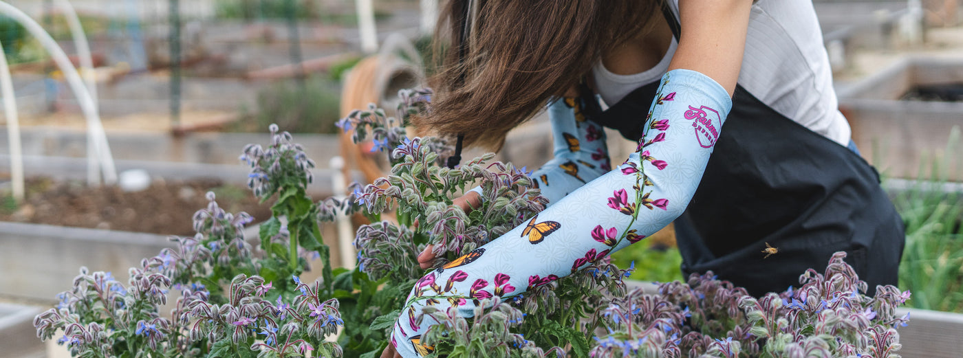 A woman in the garden tending to her flower bed wearing protective sleeves with monarch butterflies on them. 